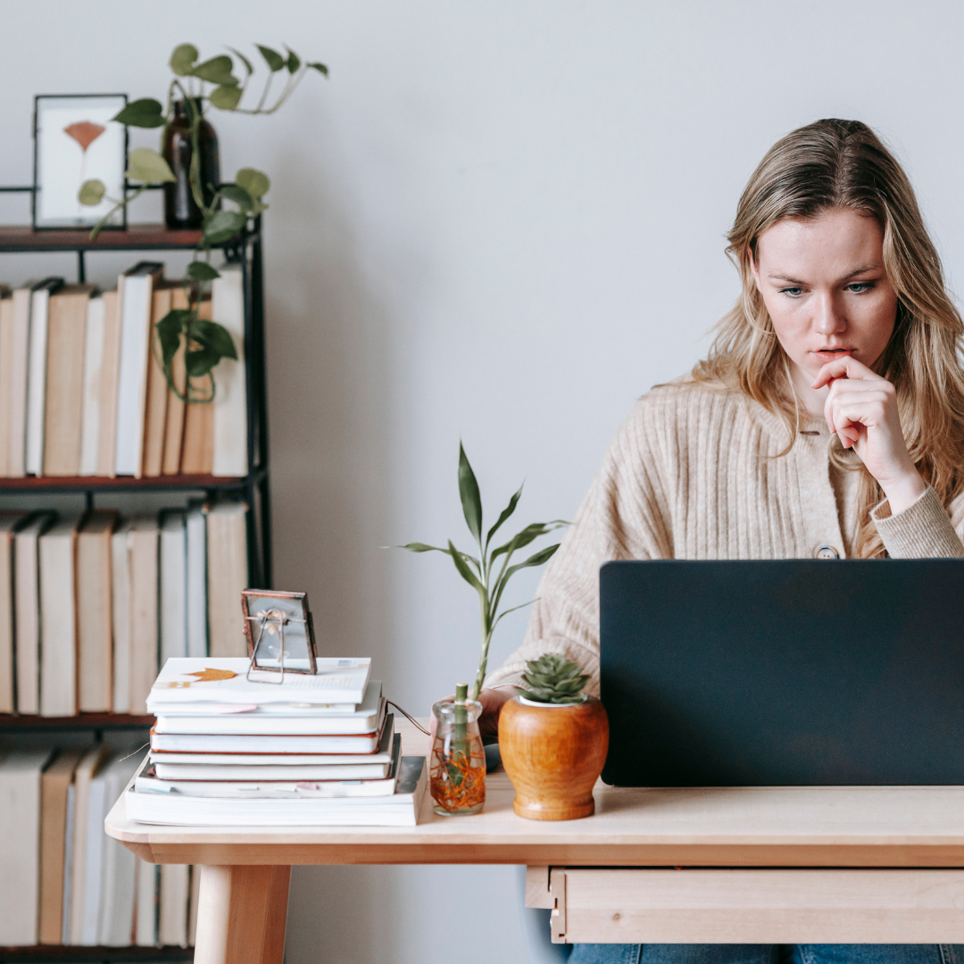 Woman on laptop with a pile of books