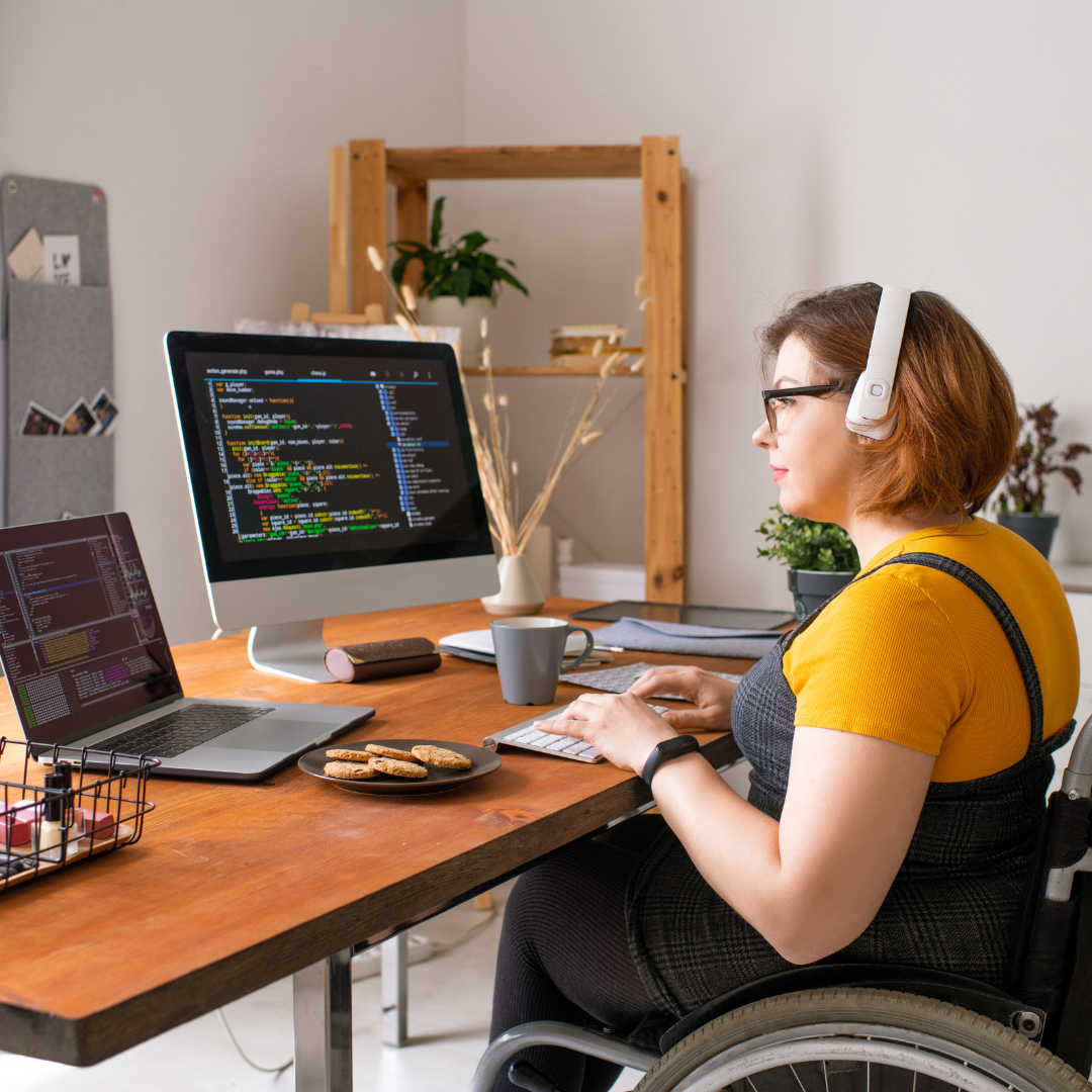 woman in a wheelchair looking at two screens with ear phones on