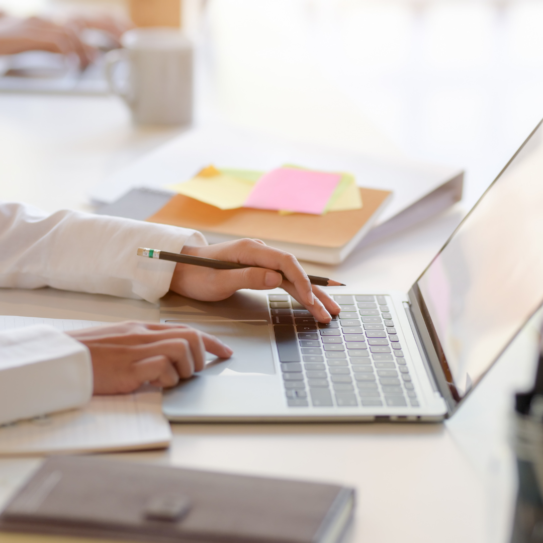 image of laptop and hands holding a pencil with post it notes and books on the table