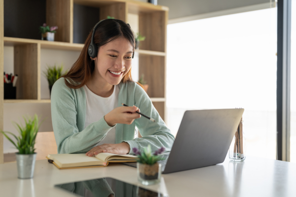 Woman sat at desk with laptop, wearing headphones on a video call