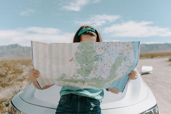 Photo of girl reading a map sat on a car