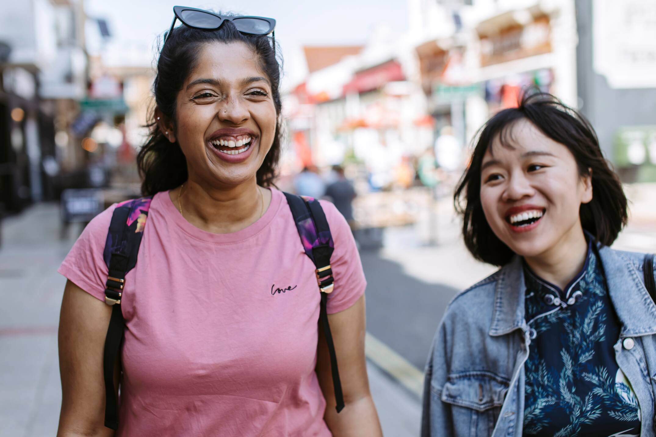 Image shows two students laughing with each other while walking down a street.