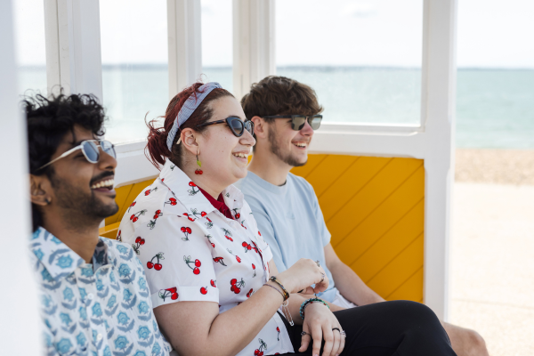 Image of 3 students sat near beach laughing
