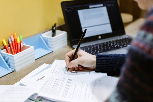 Image shows a student's laptop and worksheets.