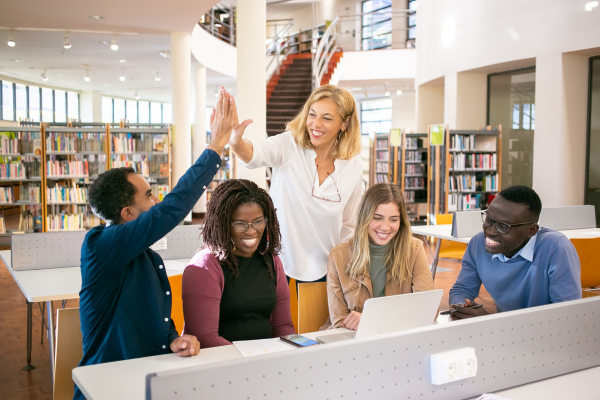 image of academic high-fiving students sat in a library