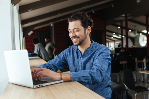 Image of man smiling, sat at desk using a laptop