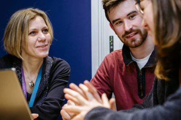 Image of three people sat round laptop in discussion