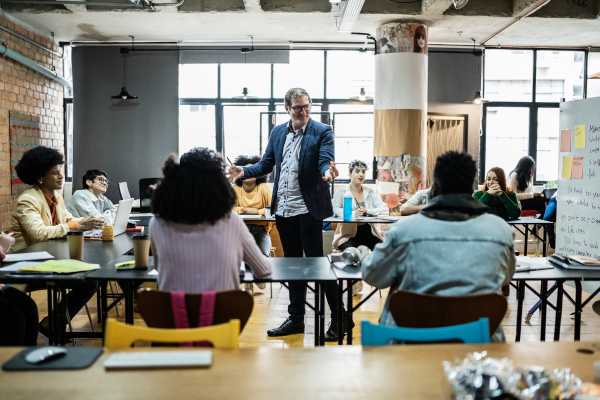 image of lecturer stood in middle of classroom surrounded by students teaching