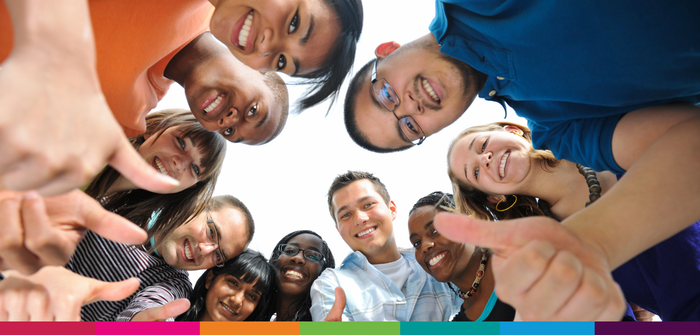 Image of multiple students stood in a circle looking down smiling with their thumbs up