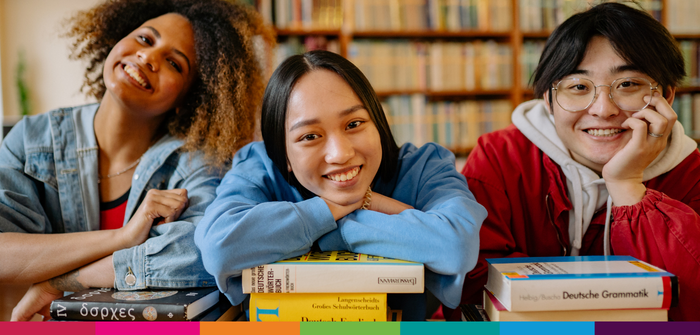 Image of three people sat leaning on books smiling ahead at camera
