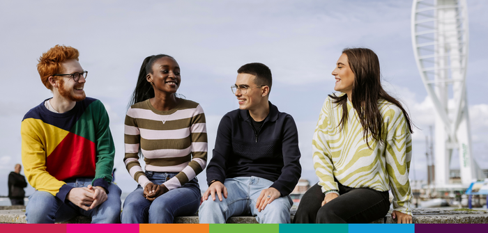 Image of four students sat on wall chatting, with Spinnaker Tower in the background
