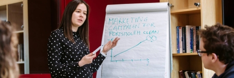 Image shows woman in front of a whiteboard discussing a marketing campaign