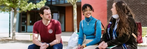 Image of three students sat outside talking to each other