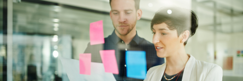 Image of 2 people collaborating on a clear board with post-it notes