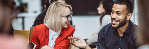 Image of two colleagues sat down and in conversation, both are smiling